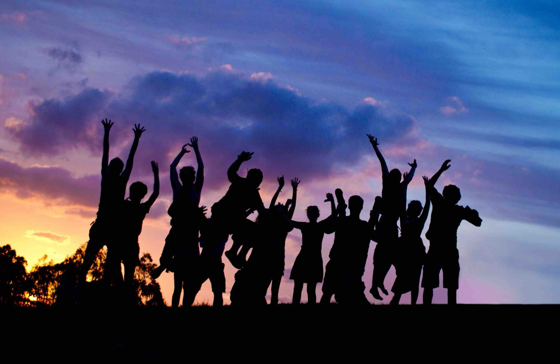 A silhouette of a group of kids jumping up, with the sunset behind them